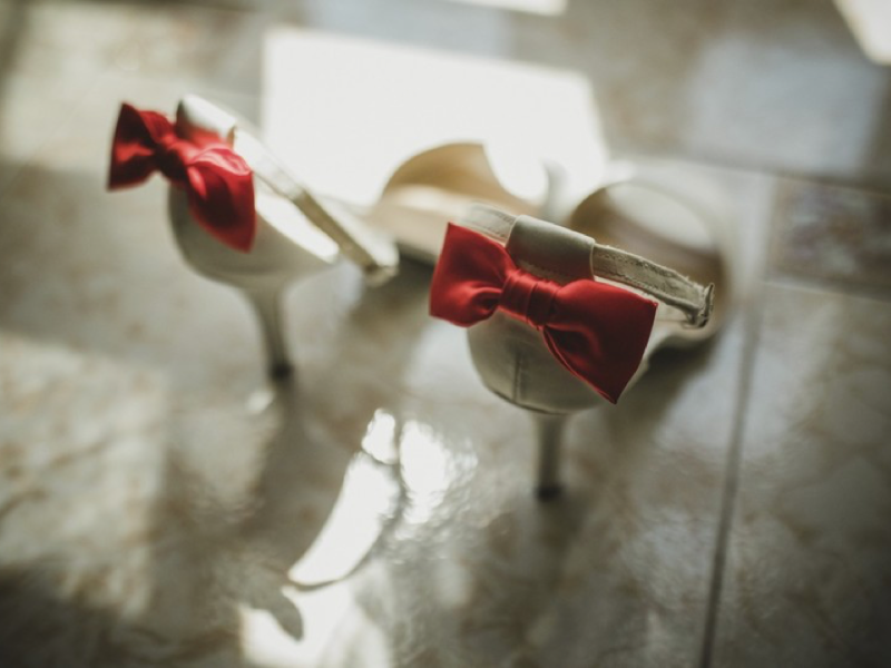 Scarpe da sposa bianche con fiocchi rossi su un pavimento illuminato
