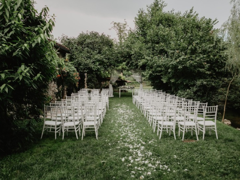 Allestimento per cerimonia di matrimonio all'aperto con sedie bianche e petali lungo il corridoio